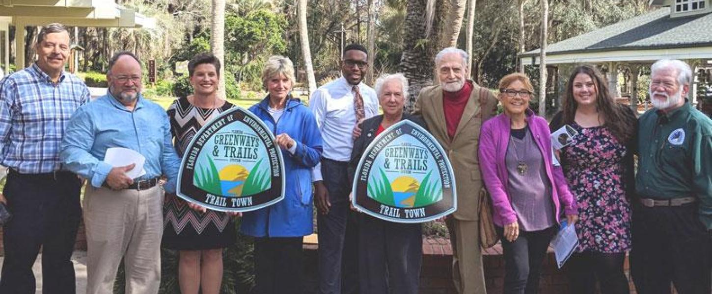A group of people posing for a picture with their trail town plaque.